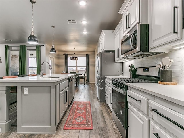 kitchen featuring decorative backsplash, a kitchen island with sink, stainless steel appliances, light countertops, and a sink