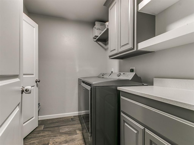 laundry area featuring dark wood-type flooring, washing machine and clothes dryer, cabinet space, and baseboards