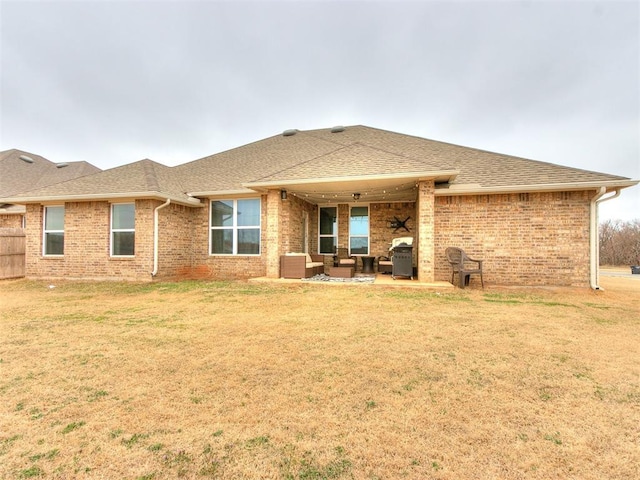 back of property with a yard, a patio, brick siding, and roof with shingles