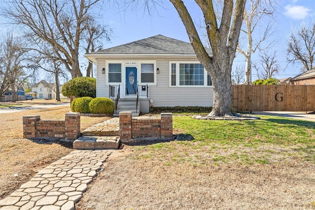 bungalow-style house featuring a shingled roof, fence, and a front lawn