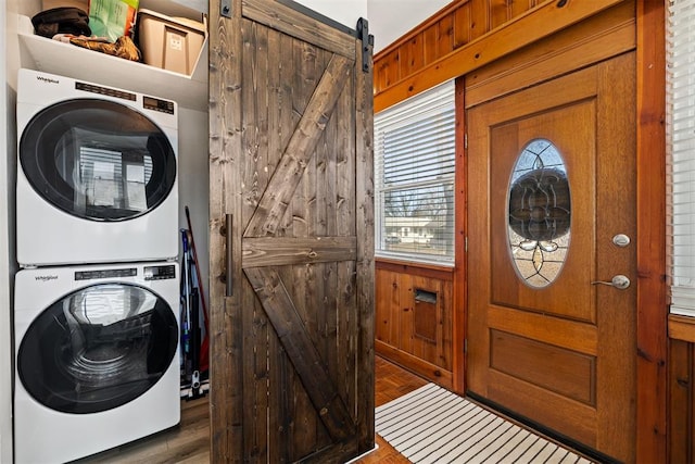 clothes washing area featuring wooden walls, a barn door, and stacked washer / drying machine