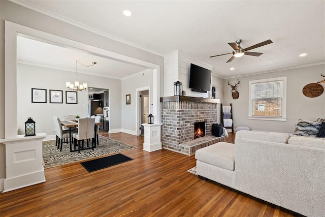 living area with ornamental molding, ceiling fan with notable chandelier, a fireplace, and wood finished floors