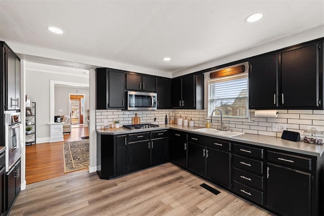 kitchen featuring appliances with stainless steel finishes, light countertops, dark cabinetry, and a sink