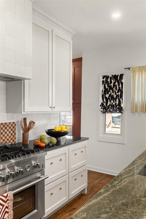 kitchen with high end stove, white cabinetry, decorative backsplash, and dark wood-style flooring