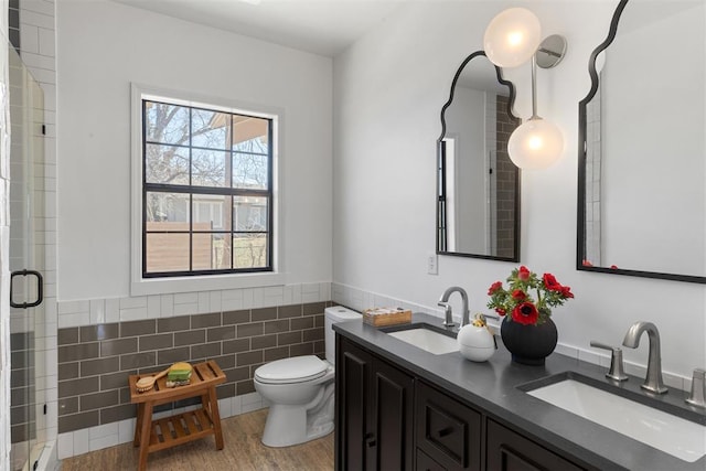 full bathroom with a stall shower, a wainscoted wall, a sink, and tile walls