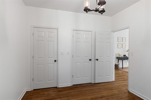 unfurnished bedroom with dark wood-style floors, a chandelier, and baseboards