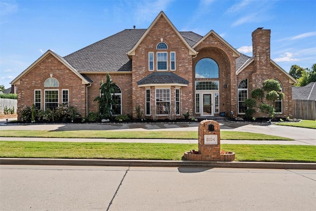 traditional-style house featuring brick siding, a chimney, a shingled roof, a front yard, and fence