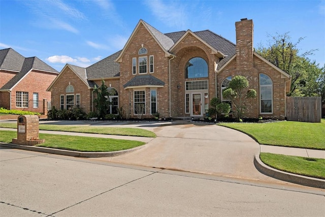 view of front of property featuring brick siding, a chimney, roof with shingles, fence, and a front yard