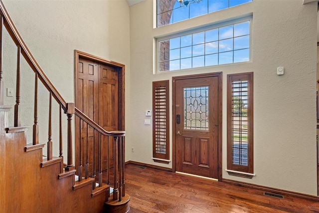 foyer featuring a towering ceiling, wood finished floors, visible vents, and baseboards