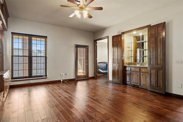 empty room with dark wood finished floors, a ceiling fan, and baseboards