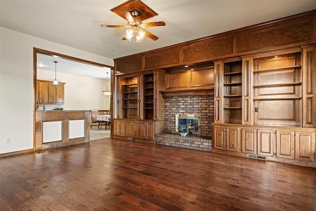 unfurnished living room with ceiling fan, visible vents, built in features, a brick fireplace, and dark wood finished floors