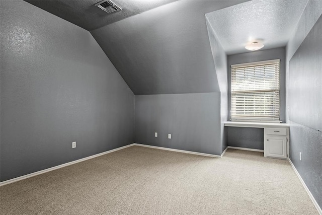 bonus room featuring carpet floors, visible vents, built in study area, a textured ceiling, and baseboards