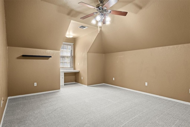 additional living space featuring carpet floors, visible vents, a ceiling fan, vaulted ceiling, and built in study area