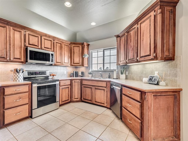 kitchen featuring light tile patterned floors, appliances with stainless steel finishes, a sink, light countertops, and backsplash