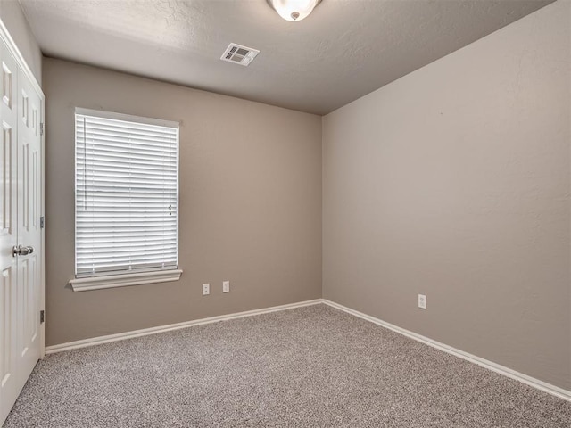 carpeted empty room featuring visible vents, a textured ceiling, and baseboards