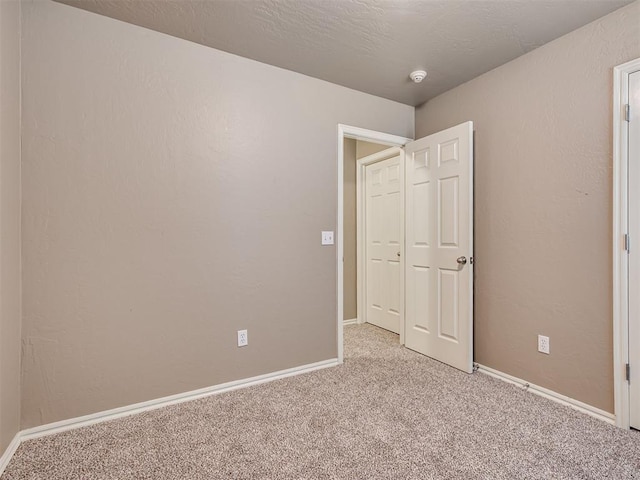 unfurnished bedroom featuring a textured wall, baseboards, a textured ceiling, and light colored carpet