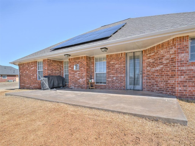 rear view of property featuring a shingled roof, roof mounted solar panels, a patio, and brick siding