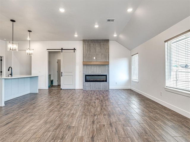 unfurnished living room with a barn door, visible vents, dark wood finished floors, baseboards, and a tile fireplace