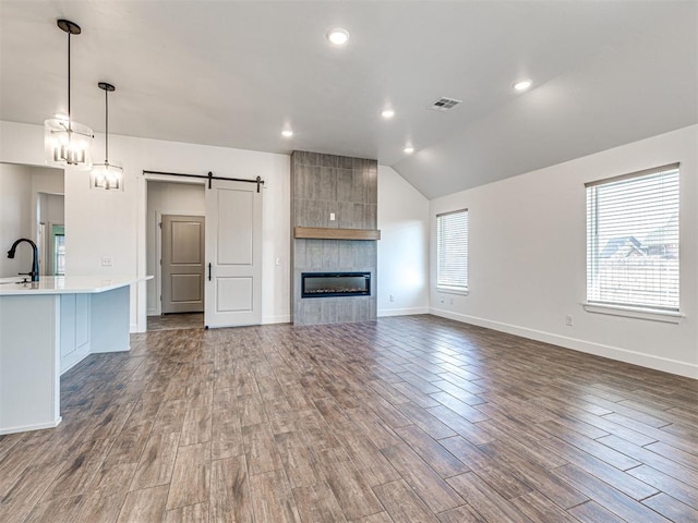 unfurnished living room featuring a barn door, visible vents, lofted ceiling, dark wood-type flooring, and a sink