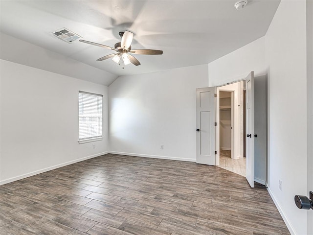 unfurnished room featuring baseboards, visible vents, a ceiling fan, wood finished floors, and vaulted ceiling