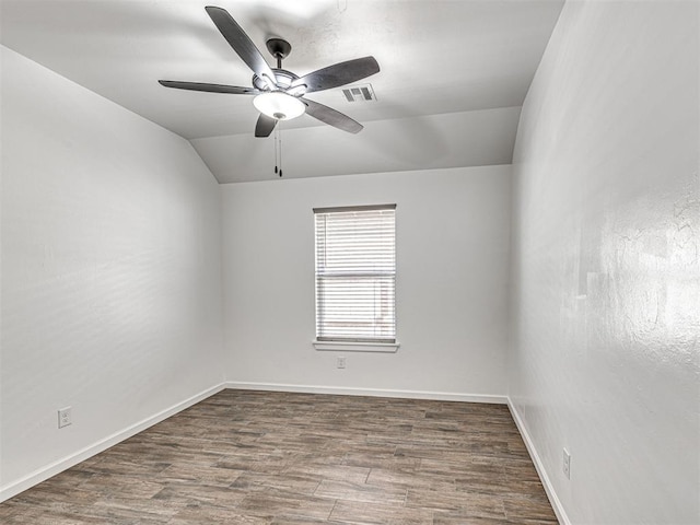 empty room with baseboards, visible vents, vaulted ceiling, and wood finished floors