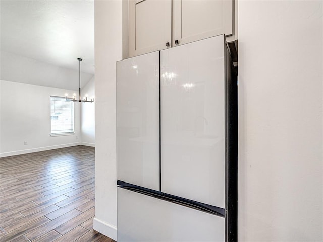 interior space featuring dark wood-style floors, lofted ceiling, freestanding refrigerator, a chandelier, and baseboards