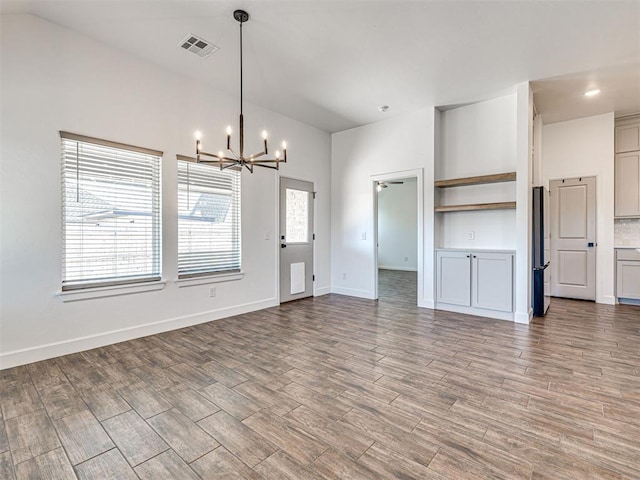 unfurnished living room with lofted ceiling, visible vents, wood finished floors, a chandelier, and baseboards