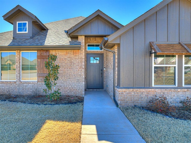 view of exterior entry featuring brick siding, board and batten siding, and a shingled roof