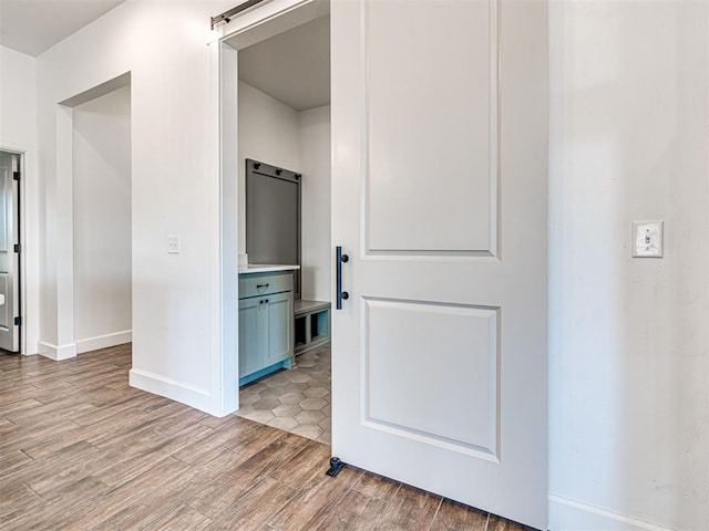 corridor featuring light wood-type flooring, a barn door, and baseboards