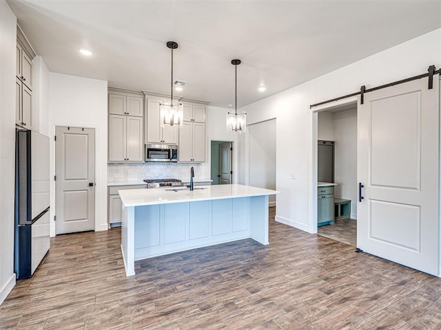 kitchen with freestanding refrigerator, wood finished floors, stainless steel microwave, and a barn door