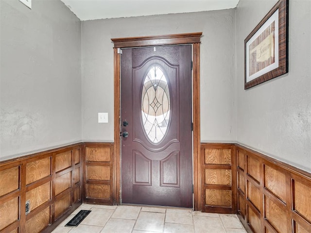 foyer entrance with a wainscoted wall, light tile patterned floors, and visible vents