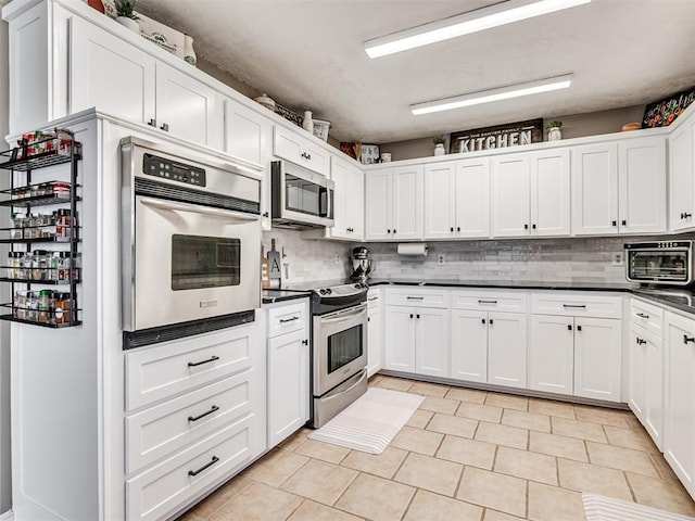 kitchen with stainless steel appliances, dark countertops, a toaster, and white cabinetry