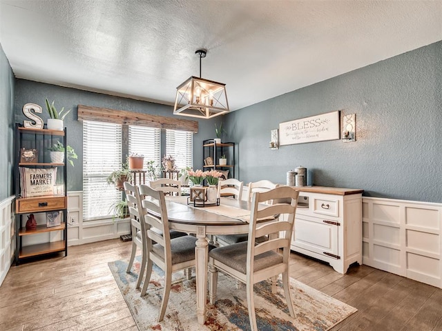 dining room featuring a textured wall, a wainscoted wall, light wood-style flooring, a textured ceiling, and a decorative wall