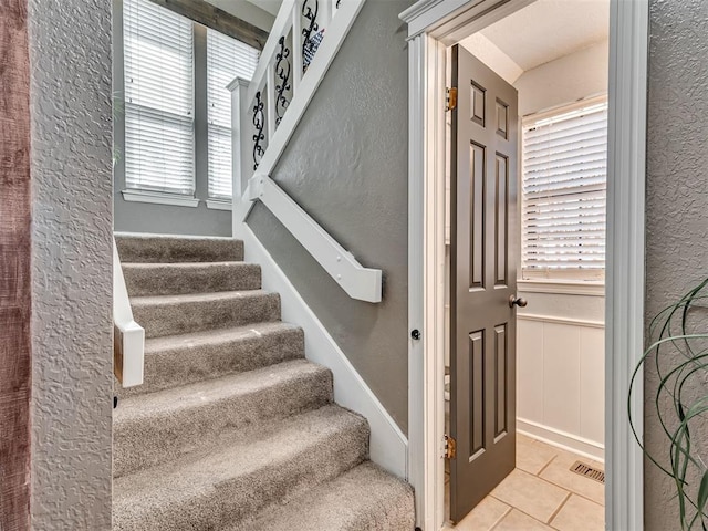 staircase featuring tile patterned flooring, wainscoting, visible vents, and a textured wall