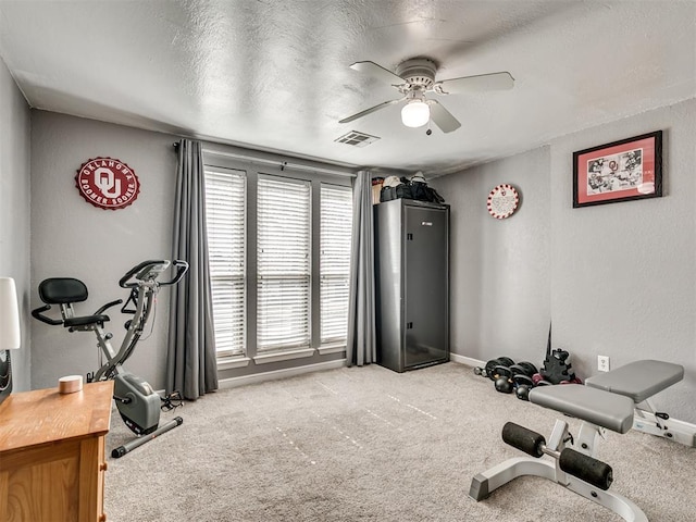 workout room featuring baseboards, visible vents, a ceiling fan, light colored carpet, and a textured ceiling