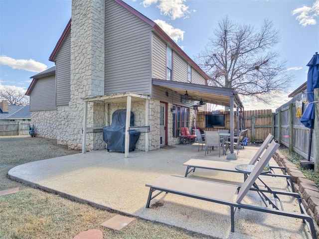 rear view of property with a patio, a chimney, stone siding, and a fenced backyard