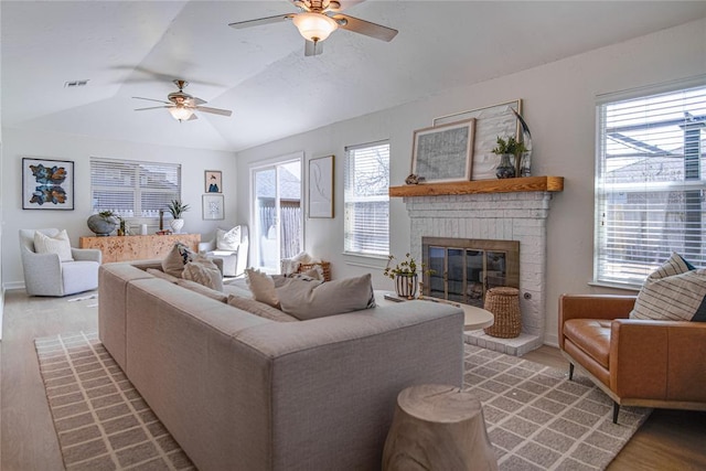 living area with plenty of natural light, a brick fireplace, light wood-style flooring, and vaulted ceiling