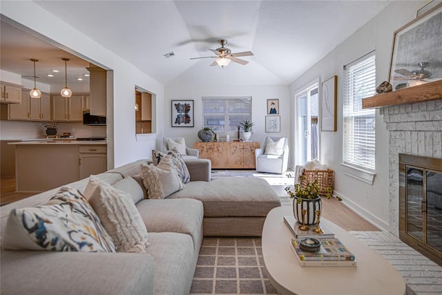 living room with a ceiling fan, visible vents, baseboards, a fireplace, and vaulted ceiling