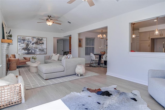 living room featuring ceiling fan with notable chandelier, visible vents, wood finished floors, and baseboards