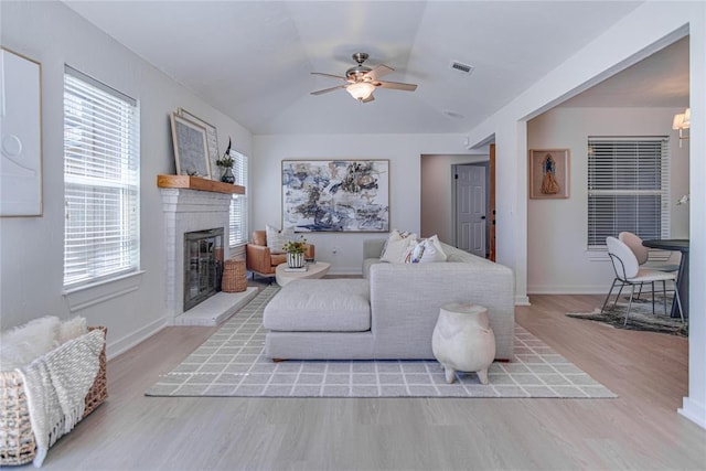 living area with visible vents, baseboards, a fireplace, ceiling fan, and light wood-style floors