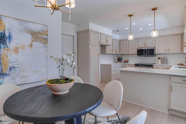 kitchen with light wood finished floors, a peninsula, a sink, light countertops, and appliances with stainless steel finishes