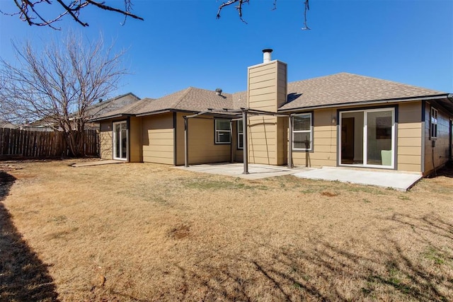 rear view of property featuring a shingled roof, fence, a chimney, a yard, and a patio area