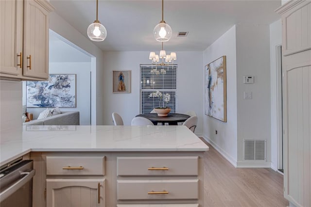 kitchen with visible vents, a peninsula, light wood-style flooring, and an inviting chandelier