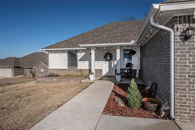 view of exterior entry with brick siding, a lawn, and a shingled roof