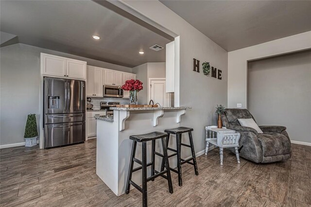 kitchen with stainless steel appliances, visible vents, dark wood-type flooring, and a breakfast bar area