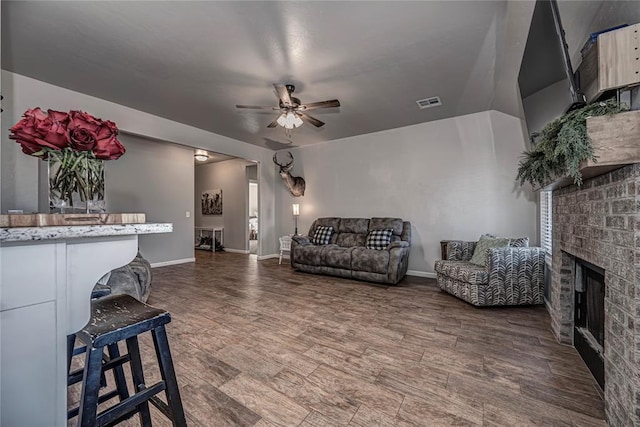 living area featuring a fireplace, wood finished floors, visible vents, baseboards, and a ceiling fan