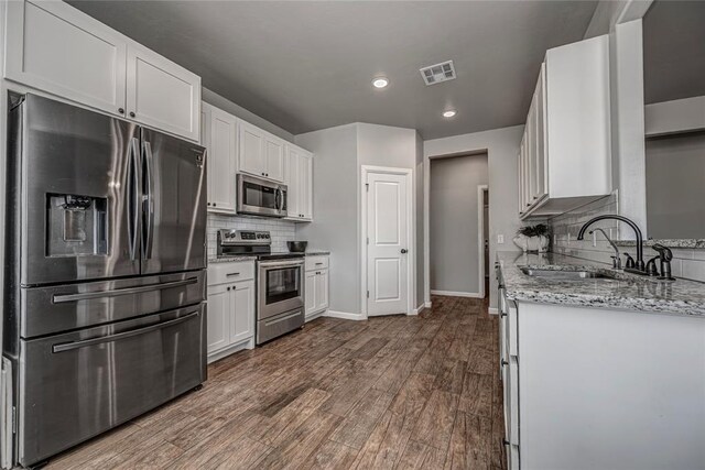 kitchen featuring stainless steel appliances, a sink, visible vents, baseboards, and dark wood finished floors