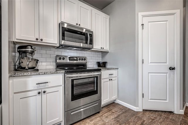 kitchen with white cabinets, appliances with stainless steel finishes, dark wood-style flooring, light stone countertops, and backsplash