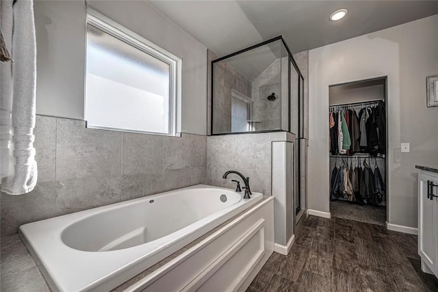 bathroom featuring baseboards, wood finished floors, a garden tub, a walk in closet, and a shower stall