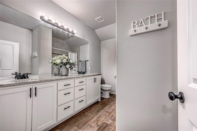 bathroom featuring double vanity, visible vents, toilet, a sink, and wood finished floors